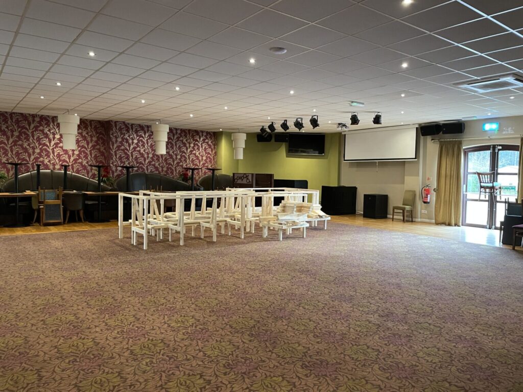 Inside a hall, with red carpet and white chairs