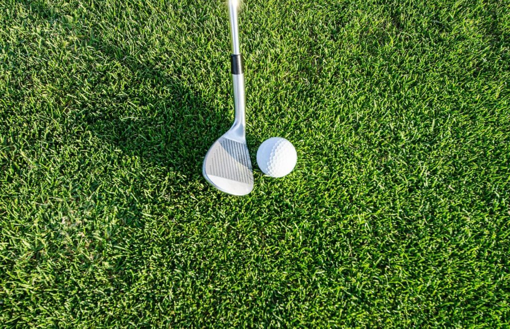 A golf stick and ball next to each other on a background of grass