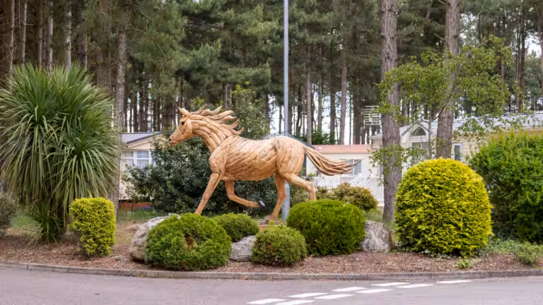 A wooden horse statue in the middle of bushes