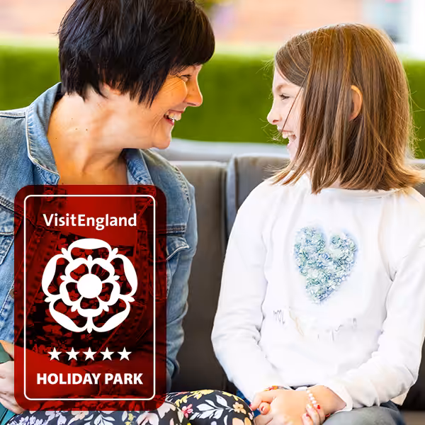 A mother and her daughter sat on a bench in a Don Amott Holiday park. With a VisitEngland award sticker