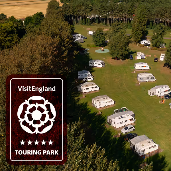 A field with caravans and motorhomes parked on. This is an aerial view of a Don Amott park, with a VisitEngland award on top
