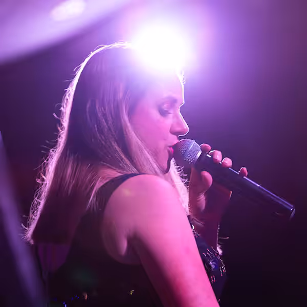 A woman singing into a microphone under purple spotlights in a Don Amott Park